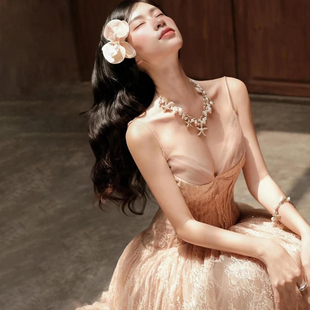 Woman in a beige dress with floral hair accessory and jewelry, sitting on a textured floor.