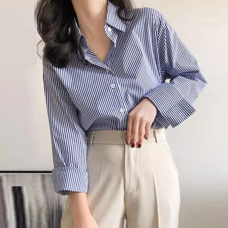 Person wearing a blue and white striped shirt with rolled-up sleeves and beige pants against a neutral background