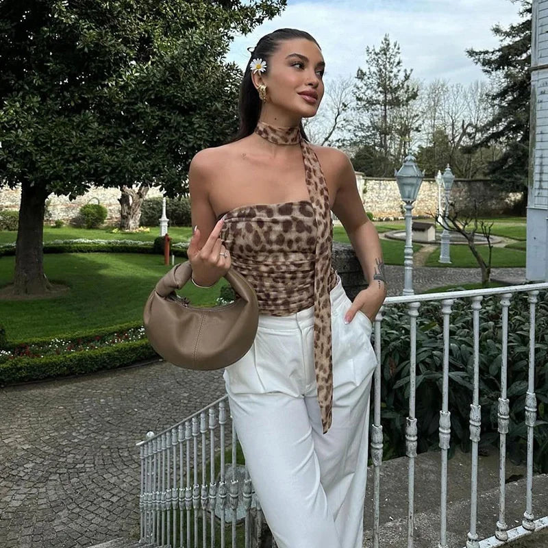 Woman in leopard print top and white pants holding a beige handbag in a garden setting