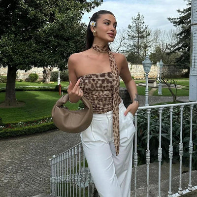 Woman in leopard print top and white pants holding a beige handbag in a garden setting