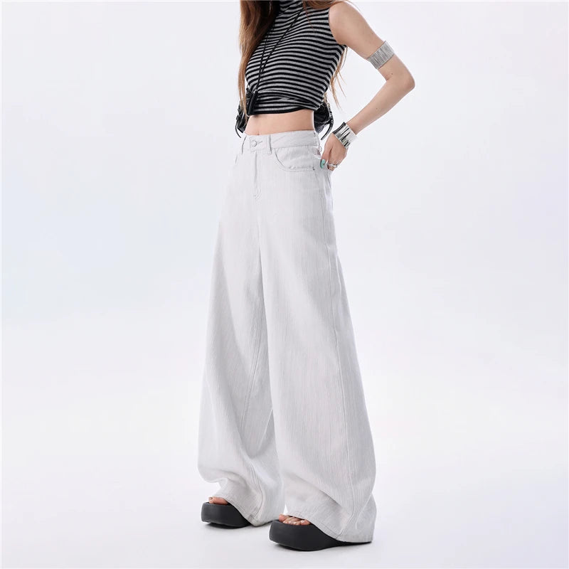 A model wearing high-waisted, wide-leg white pants paired with a black and white striped crop top and black platform sandals, shown from the waist down on a white studio background.