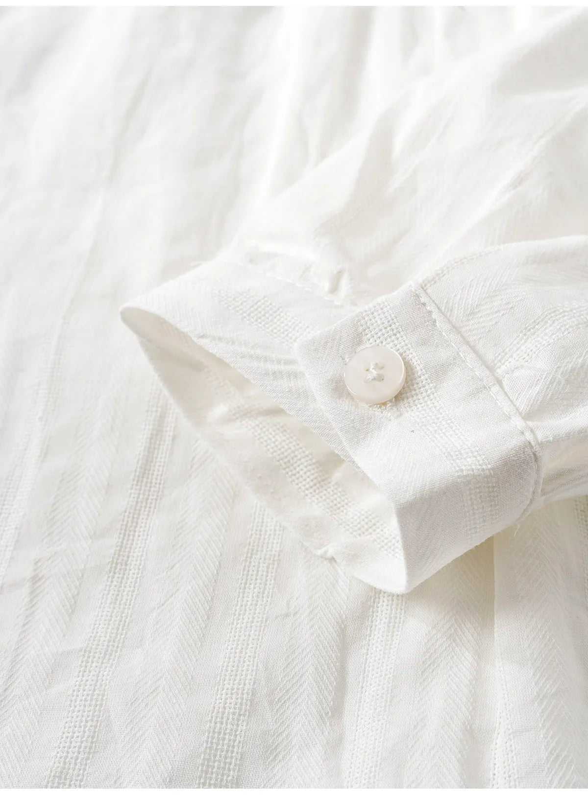 Close-up of a white textured fabric garment, showing a folded cuff with a single white button.
