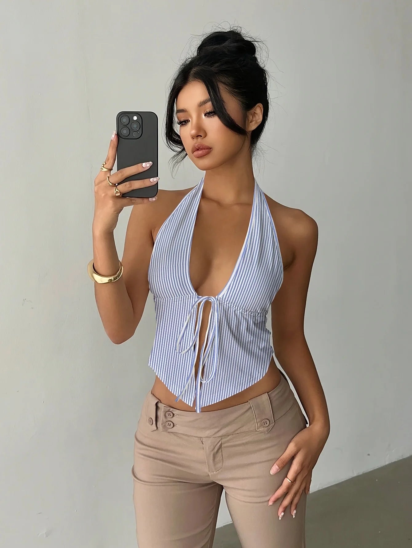 Woman taking a mirror selfie wearing a blue and white striped halter top and beige pants.
