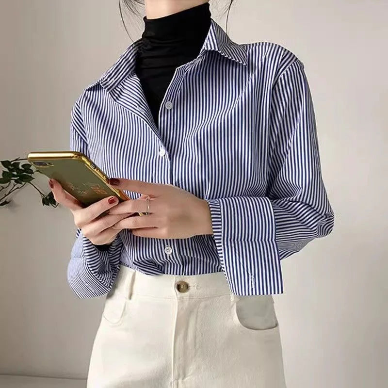 Person wearing a blue and white striped shirt holding a phone against a plain background