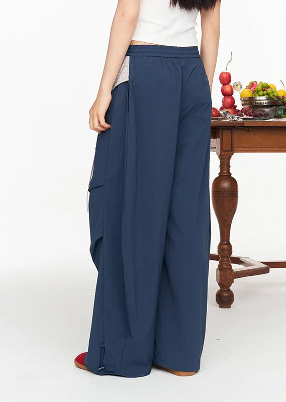 A model from the back wearing wide-leg navy blue cargo pants, shown in a studio setting with a wooden table and fruit in the background.