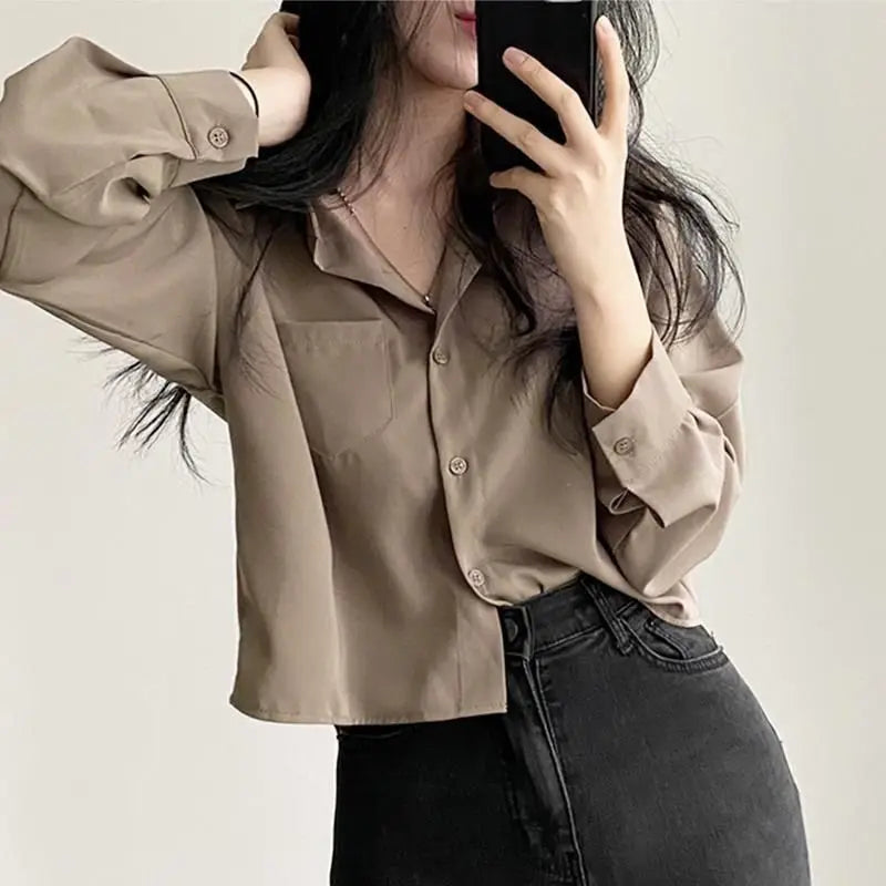 Person wearing a beige button-up shirt and black pants against a plain background