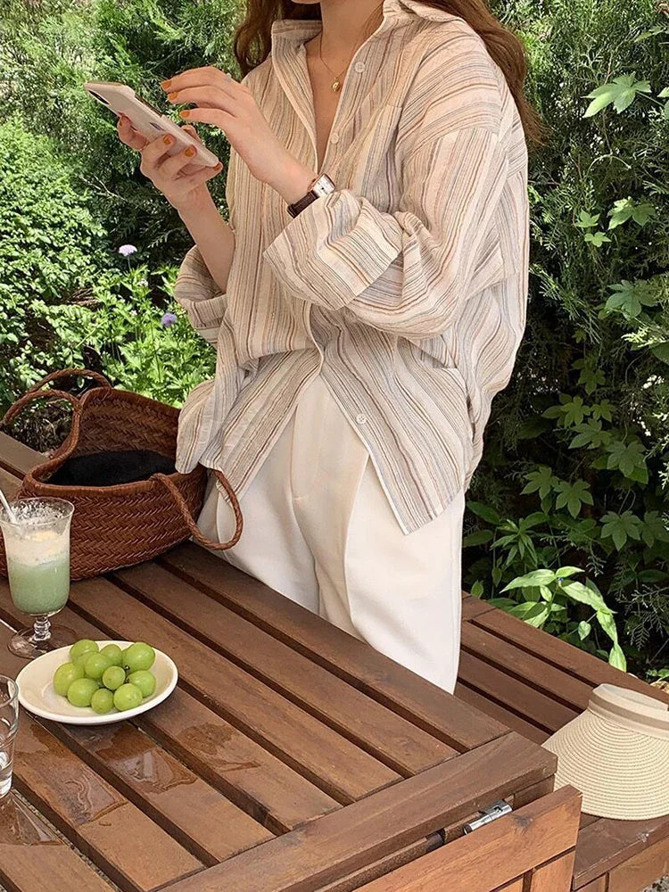 Person sitting at a wooden table outdoors, using a phone with a plate of green apples and a glass of milk on the table.