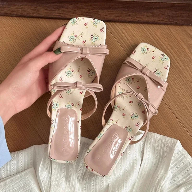 Pair of pink floral sandals with a hand holding one shoe on a wooden surface.