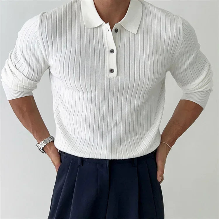 Person wearing a white ribbed sweater over a white shirt with navy pants on a plain background