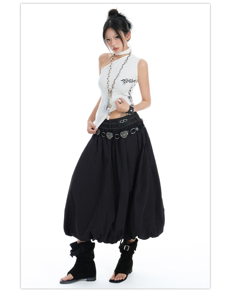 A model wearing a white sleeveless top with graphic text and a long black harem skirt with a heart-patterned belt, paired with black ankle boots, set against a plain white background.