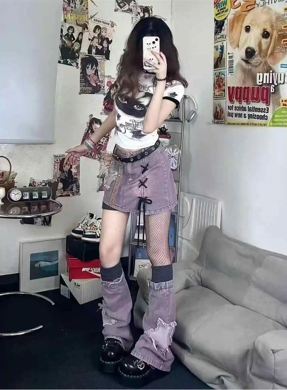 A person taking a mirror selfie in a room, wearing a white graphic t-shirt, purple denim shorts, fishnet socks, and black platform shoes. The room has a gray couch, a side table, and posters on the wall.