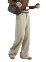 Person wearing a brown sweater, beige wide-leg pants, and holding a coffee cup against a white background