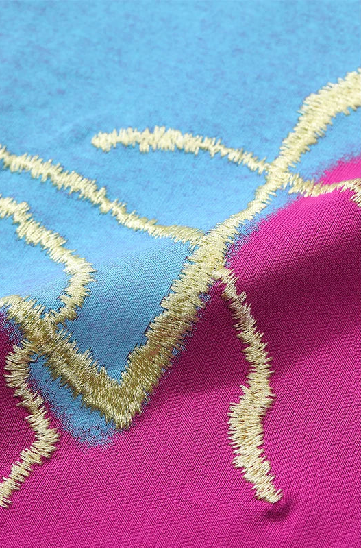 Close-up of a fabric surface with a color-blocked pattern in light blue and bright pink, separated by irregular metallic gold embroidered lines.