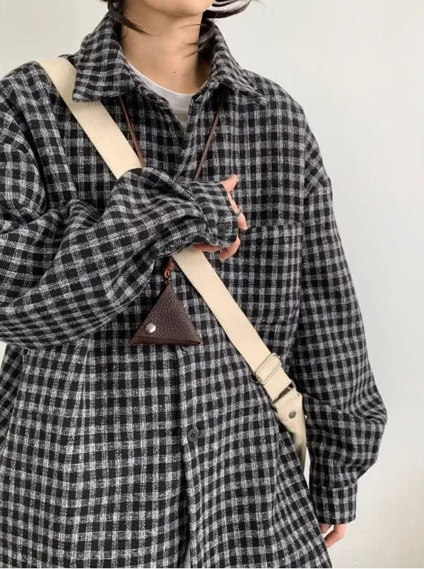 Person wearing a black and white checkered coat holding a beige crossbody bag.