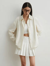 Woman wearing a cream-colored cardigan over a white top and skirt on a plain background