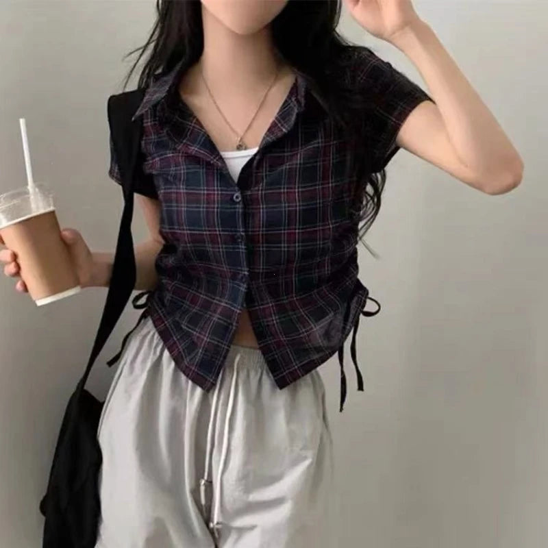 Person wearing a plaid vest and holding a drink against a plain background