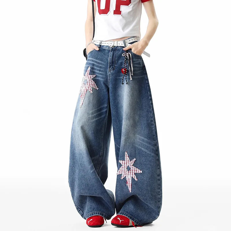 A person wearing wide-leg blue denim jeans with red-and-white star embellishments on the legs, paired with a white graphic T-shirt and red shoes, against a plain white background.