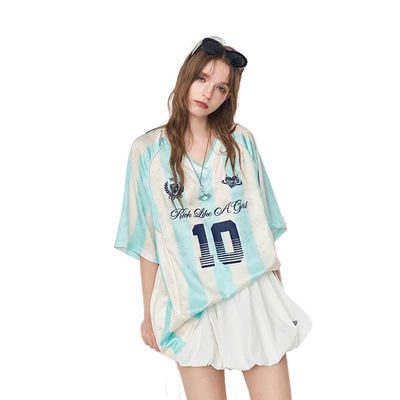 A woman modeling a light blue and white tie-dye short-sleeve t-shirt with a dark blue number 10 and 'Fish Like A Girl' text, paired with a white pleated skirt against a solid white background.