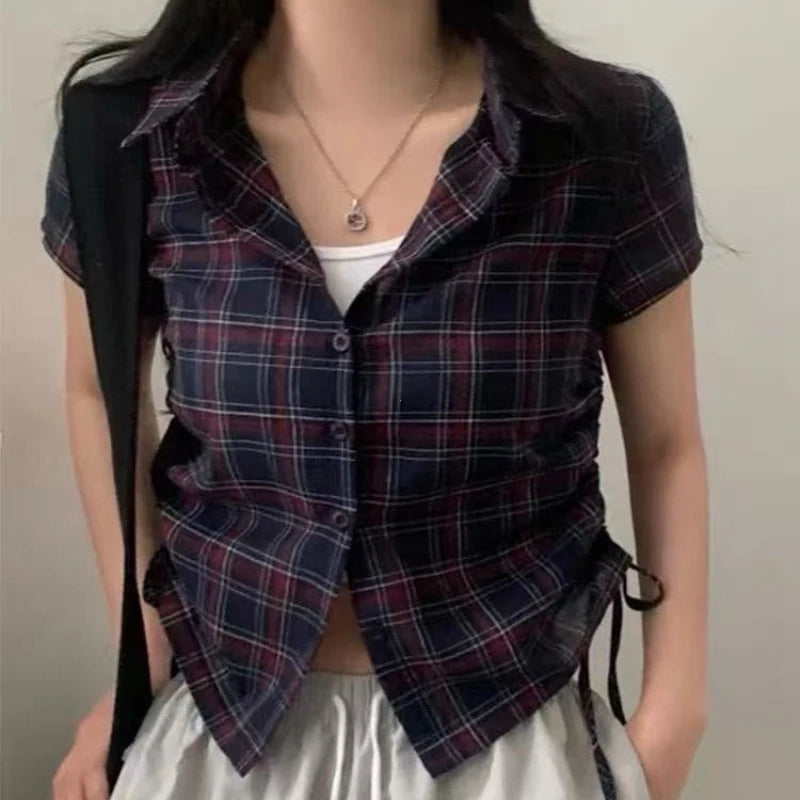 Person wearing a plaid shirt over a white top with a neutral background