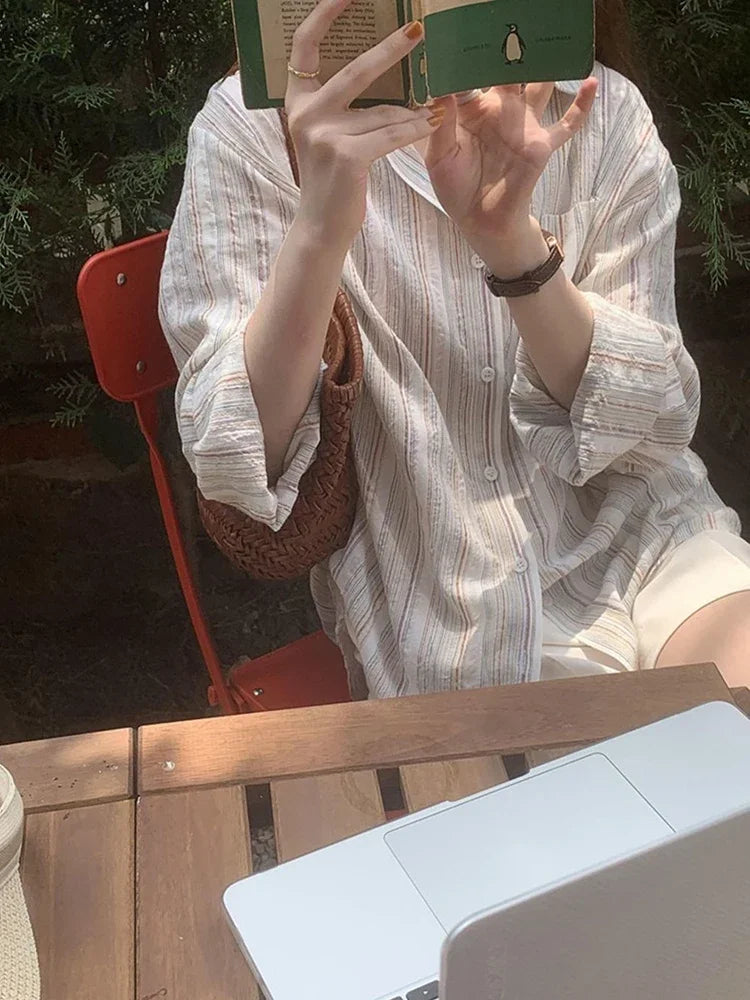 Person sitting at a wooden table outdoors, holding a phone above their head.