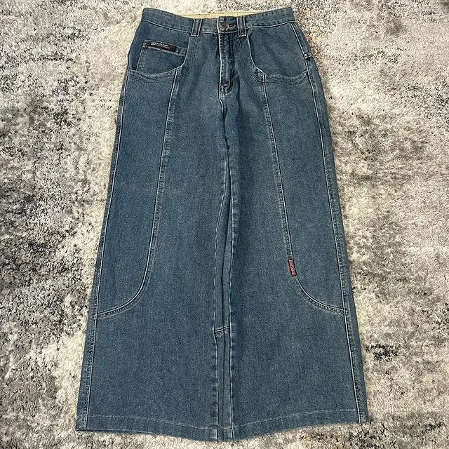 Blue denim Jeans with front slash pockets and a button fly, laid flat on a textured gray and white rug.