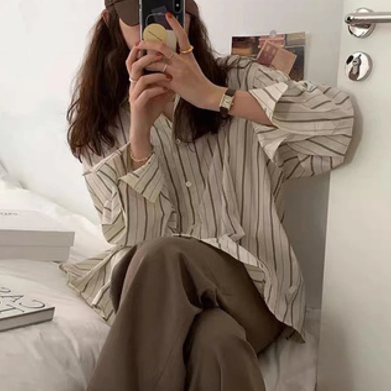 Person wearing a striped shirt and brown pants sitting on a bed.
