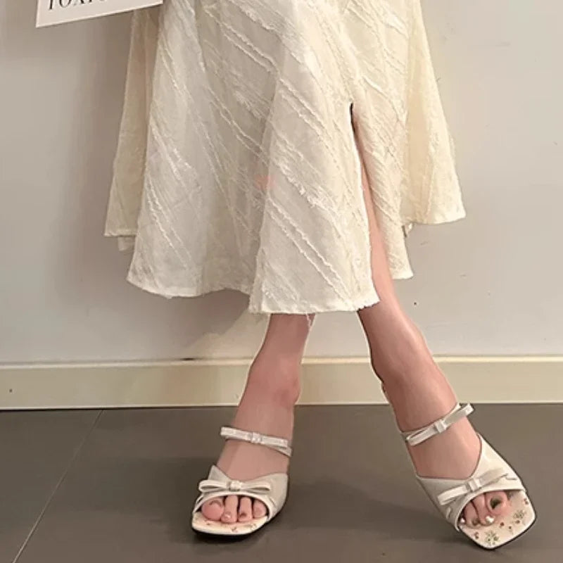 White sandals worn with a light-colored dress on a neutral background