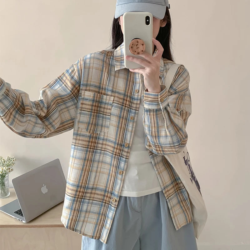 Person wearing a plaid shirt and taking a mirror selfie in a room with a laptop on a desk.