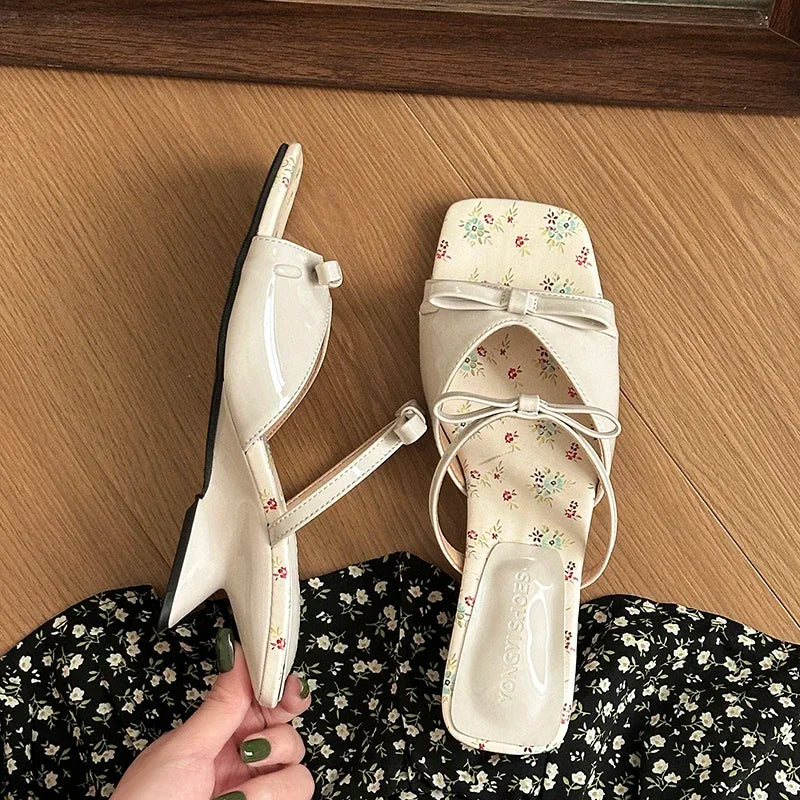 Pair of white sandals with floral patterns on a wooden floor.