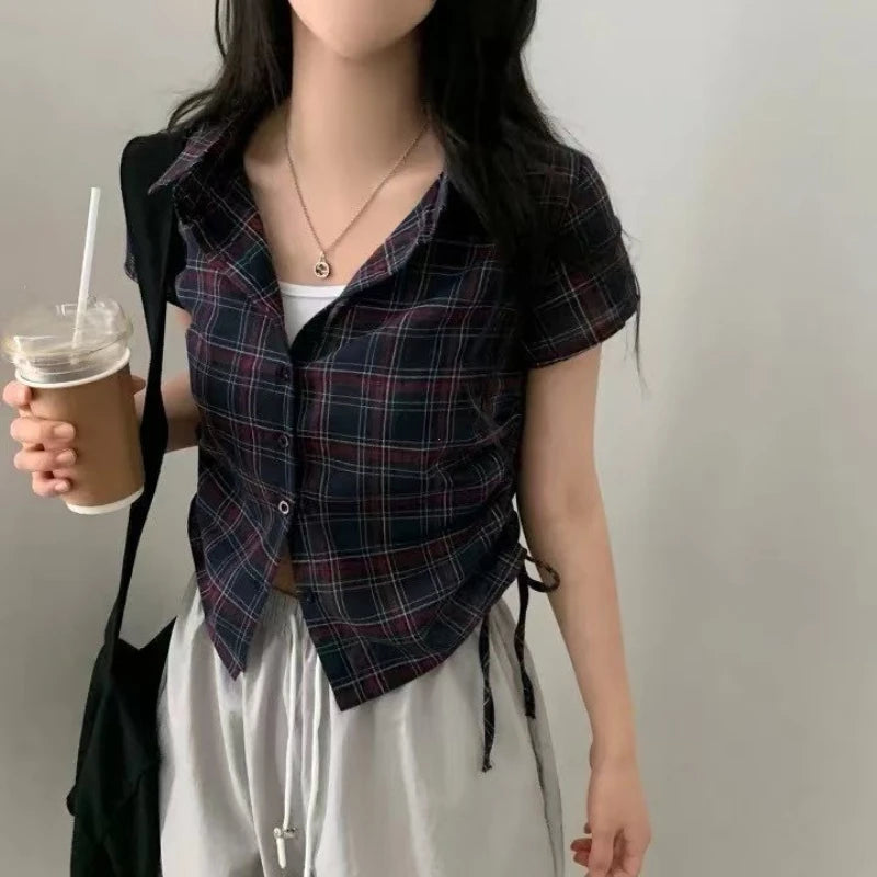 Person wearing a plaid shirt over a white top, holding a drink.