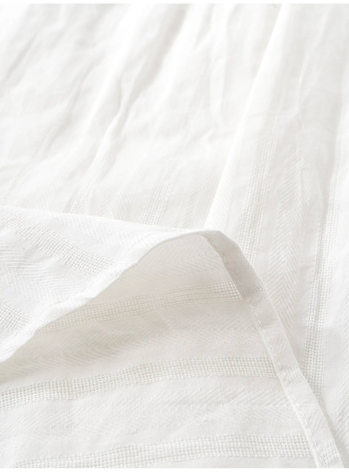 A close-up of white textured fabric with soft folds and a visible stitched edge.