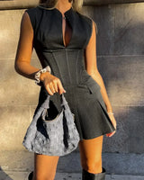 Woman wearing a black dress holding a gray handbag against a stone wall.