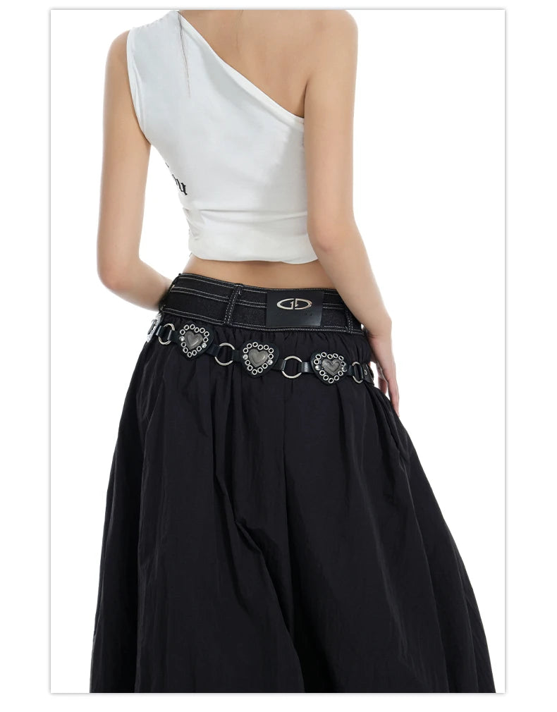 A model shown from the back wearing a white one-shoulder crop top and a black skirt with a decorative silver heart-and-ring belt.