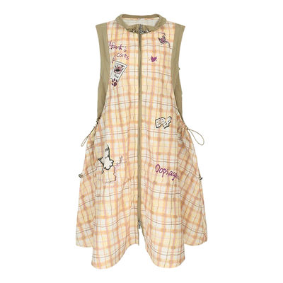 A sleeveless, front-zip A-line dress with a light peach and white plaid pattern, decorated with various cartoon stickers, patches, and handwritten text, featuring beige shoulder straps.